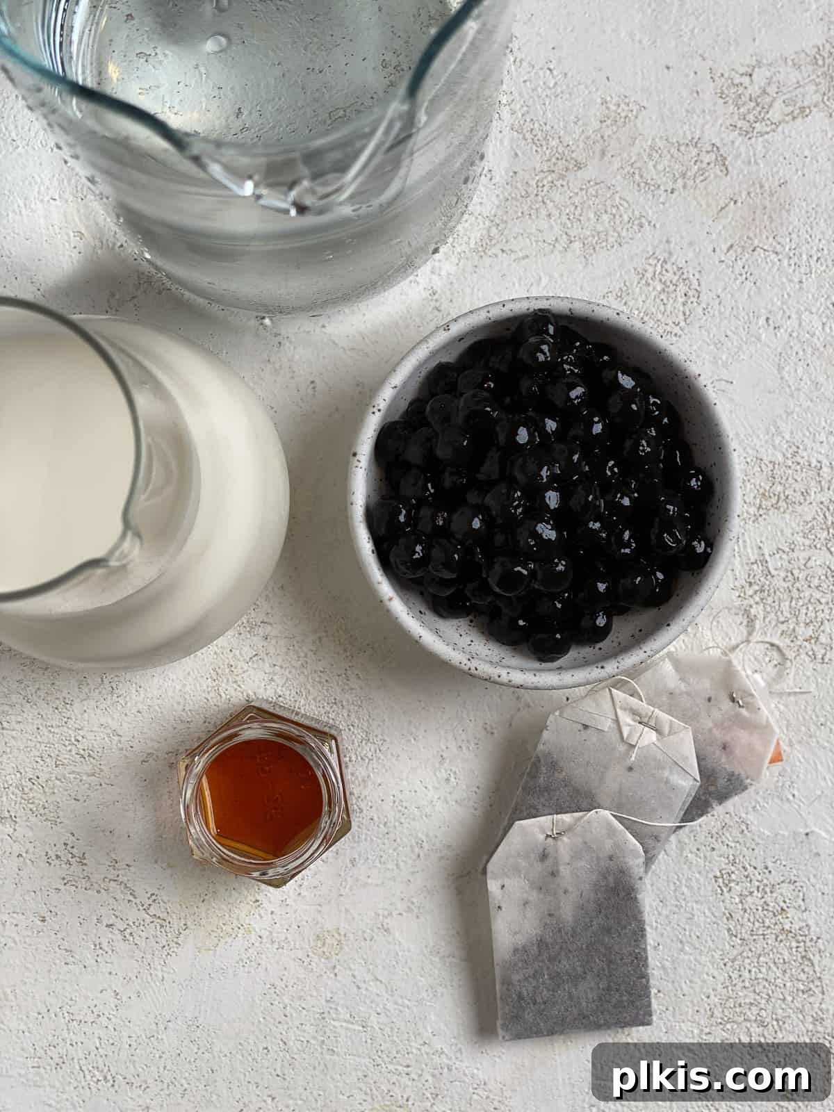 Simple Vegan Boba Bliss 3 All the essential ingredients for an Easy Vegan Bubble Tea recipe, including black tea bags, tapioca pearls, plant-based creamer, and agave, neatly arranged on a white surface.