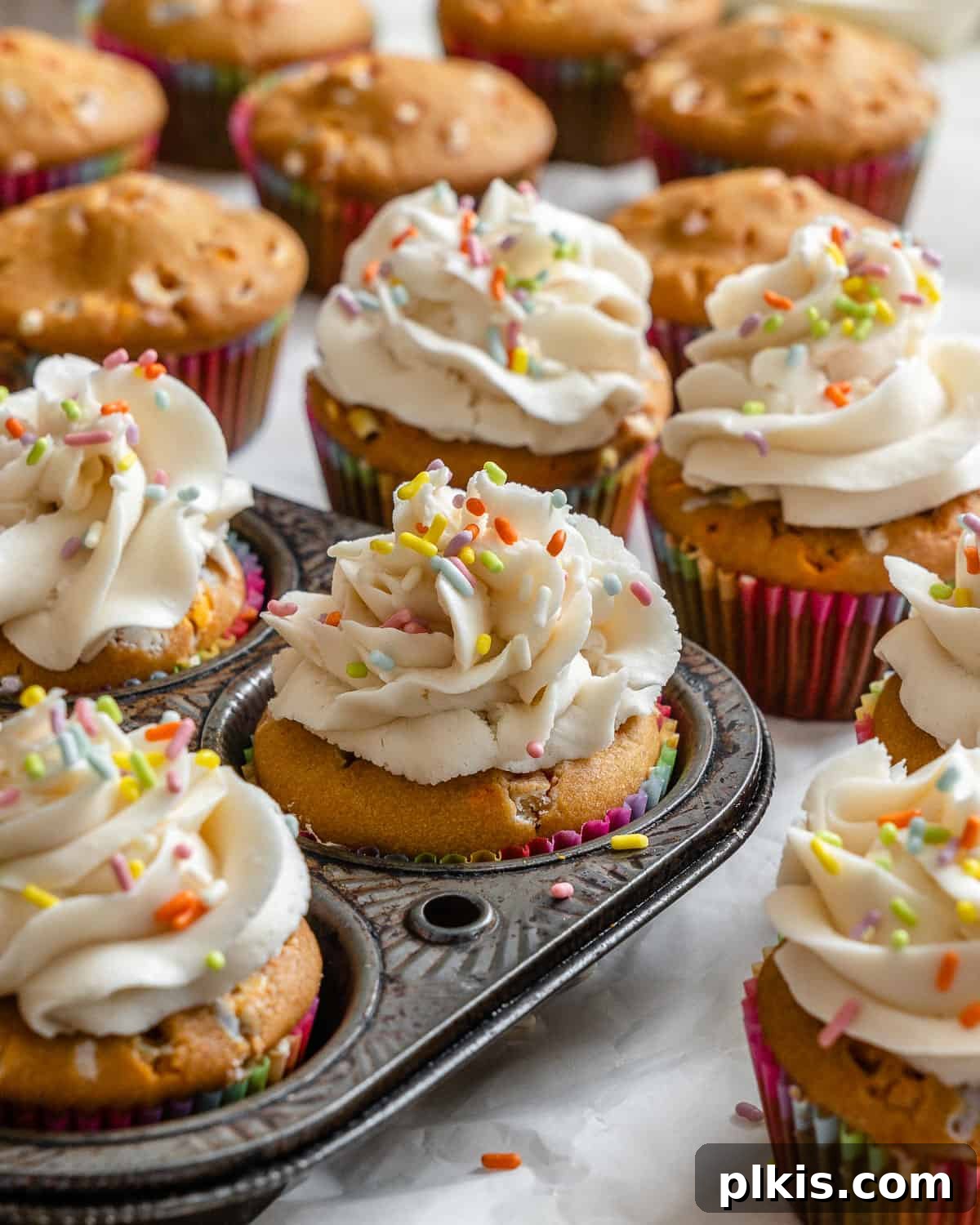Rainbow Vegan Cupcake Magic 2 Completed Vegan Funfetti Cupcakes on a pristine white surface, with a cupcake tin visible in the background.