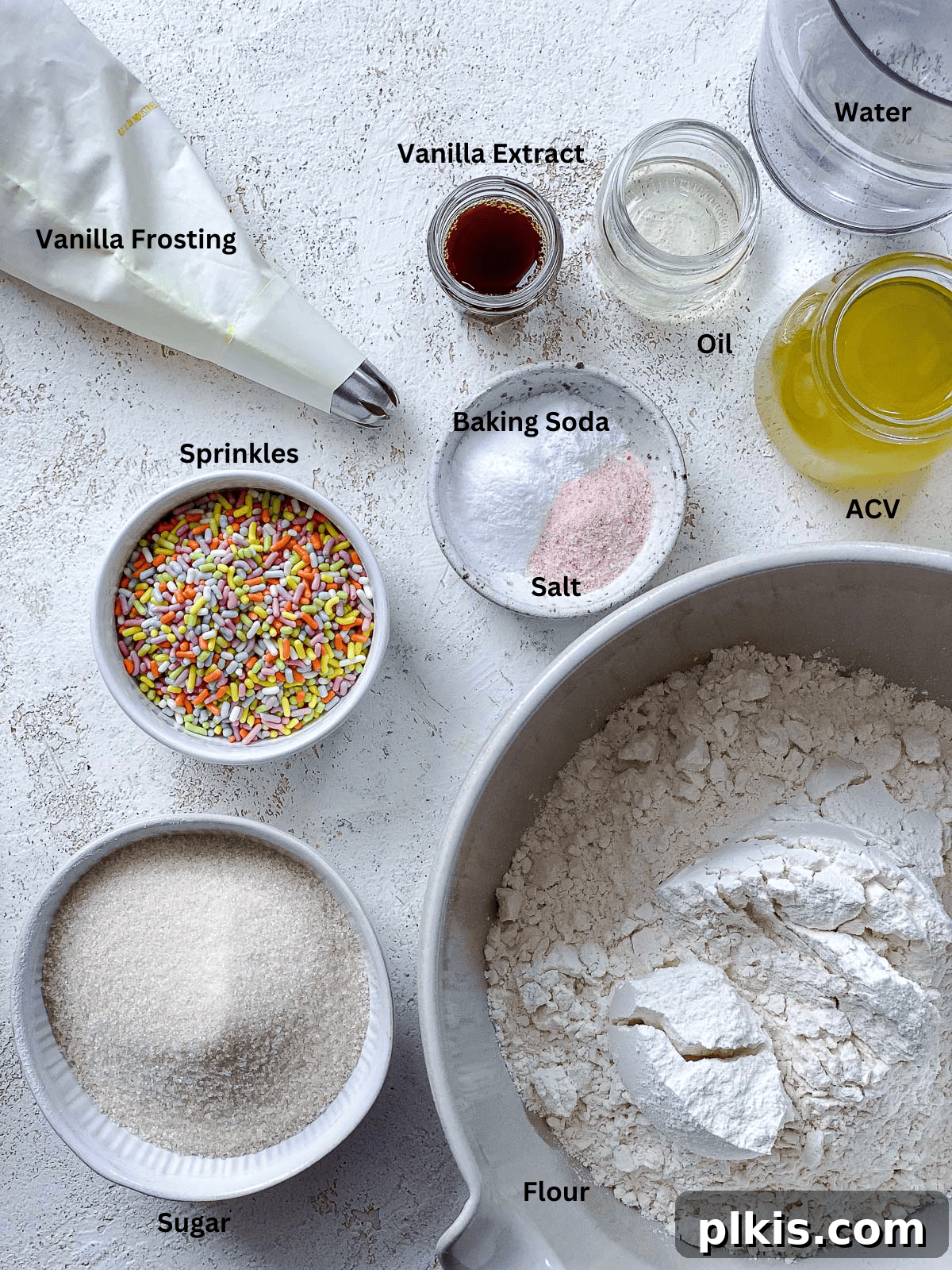Rainbow Vegan Cupcake Magic 3 A selection of ingredients for Vegan Funfetti Cupcakes, including flour, sugar, oil, vanilla extract, and colorful sprinkles, arranged aesthetically on a white surface.