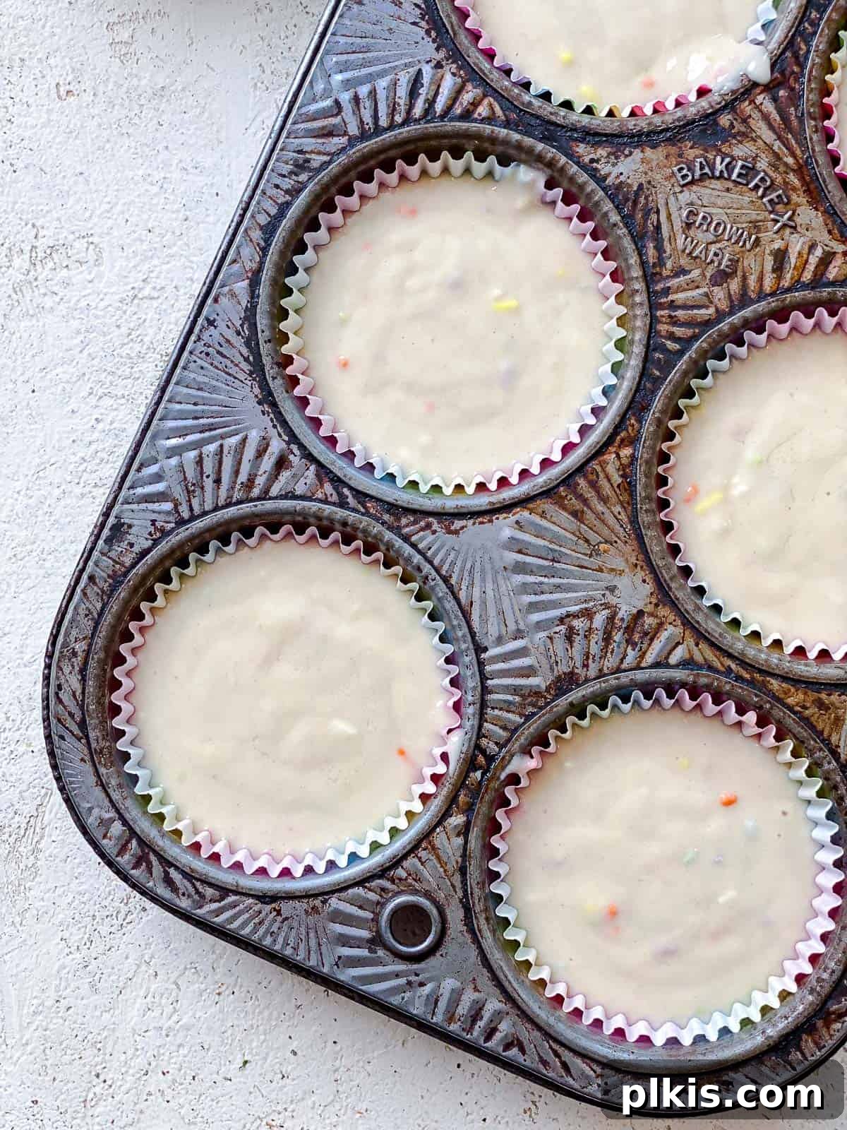 Rainbow Vegan Cupcake Magic 5 Process shot displaying cupcake batter neatly scooped into paper liners within a cupcake tin, ready for baking.
