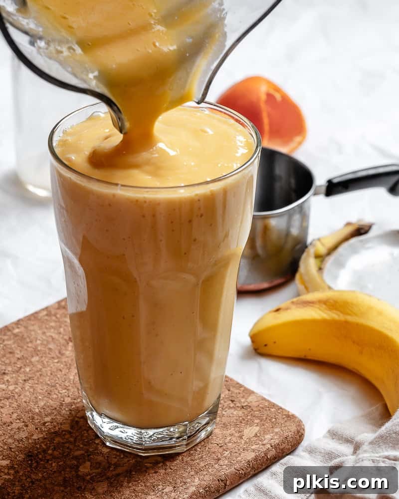 Tropical Glow Smoothie 2 A refreshing Mango Orange Smoothie being poured into a tall glass, showcasing its vibrant orange color and creamy texture.