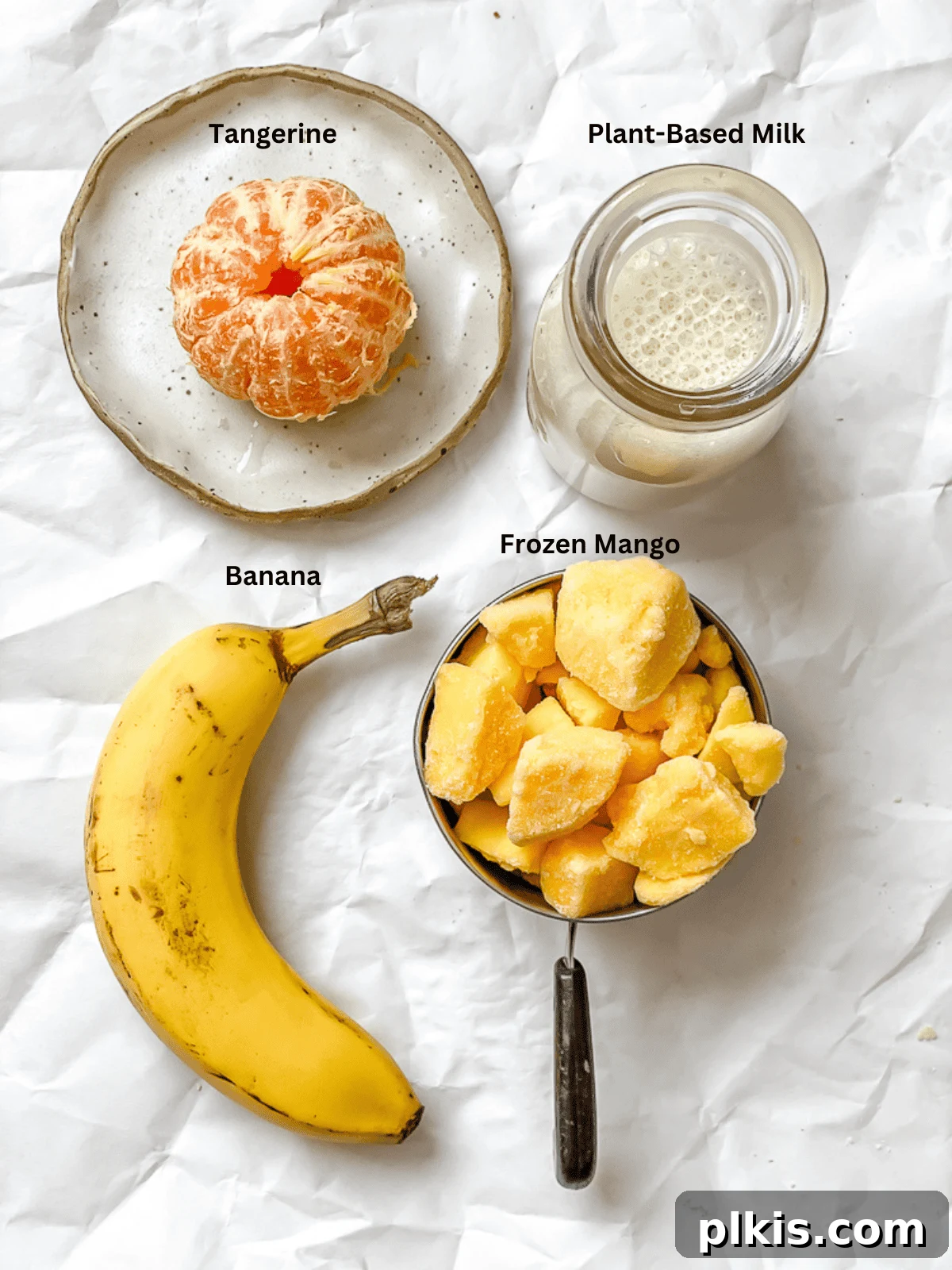 Tropical Glow Smoothie 3 Carefully measured ingredients for a Mango Orange Smoothie laid out on a clean white surface, including frozen mango, a banana, a peeled tangerine, and plant-based milk.