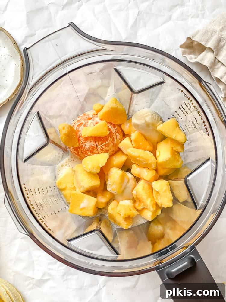 Tropical Glow Smoothie 4 Ingredients for Mango Orange Smoothie carefully placed in a high-speed blender, with liquid at the bottom and frozen fruit on top, ready for blending.
