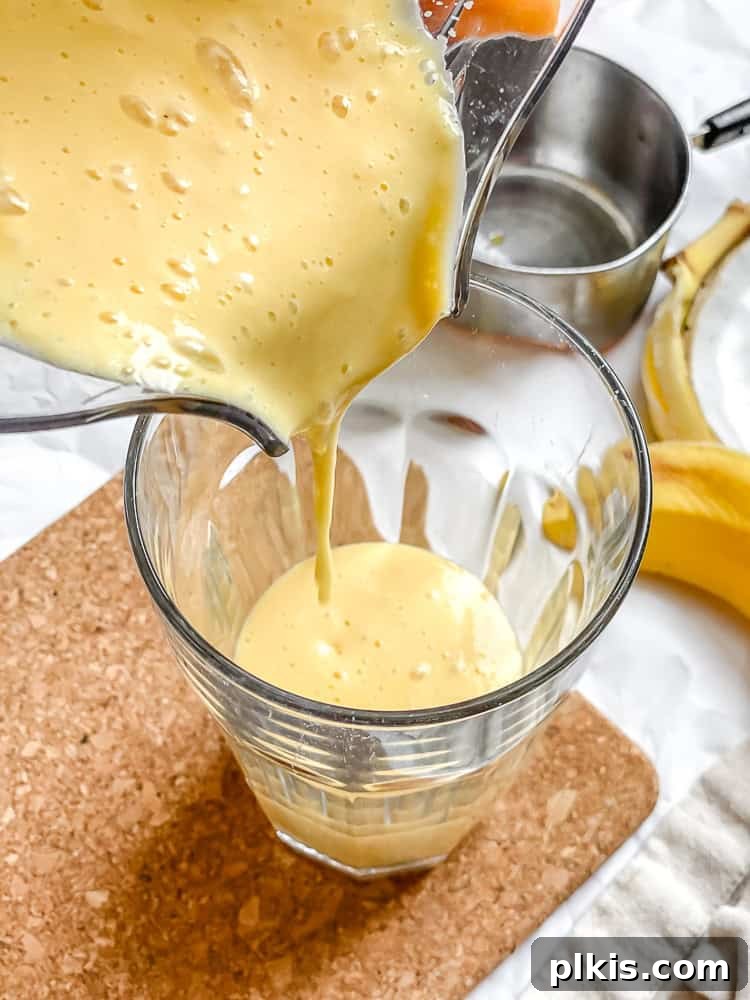 Tropical Glow Smoothie 6 A stream of rich, orange Mango Orange Smoothie pouring from a blender into a clear glass, ready to be enjoyed.