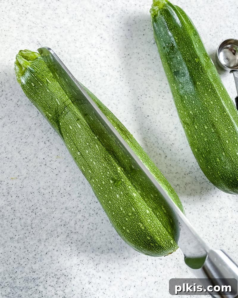 Process shot showing a zucchini being sliced lengthwise on a cutting board, preparing it for stuffing.