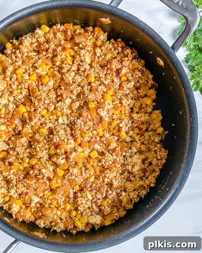 Process shot showing the taco-spiced tofu and vegetable filling cooking in a large skillet on the stovetop.