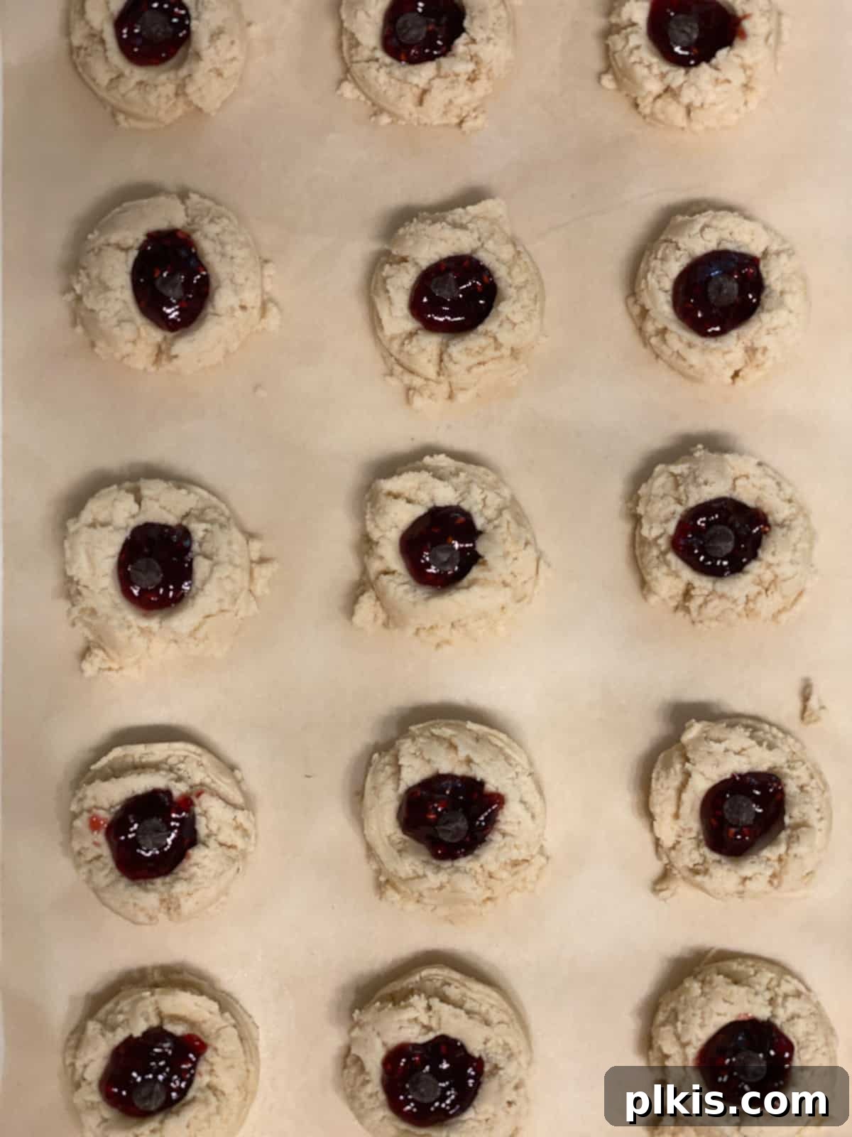 Ruby Raspberry Thumbprint Delights 17 pre baked Raspberry Jam Thumbprint Cookies scattered on a baking sheet