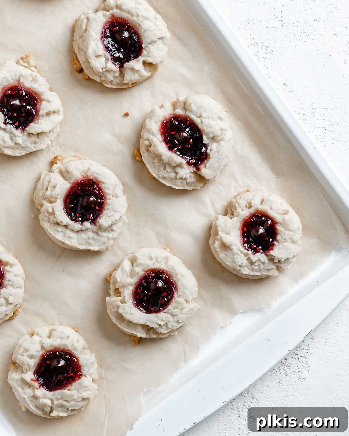 Ruby Raspberry Thumbprint Delights 19 completed Raspberry Jam Thumbprint Cookies scattered on a baking sheet