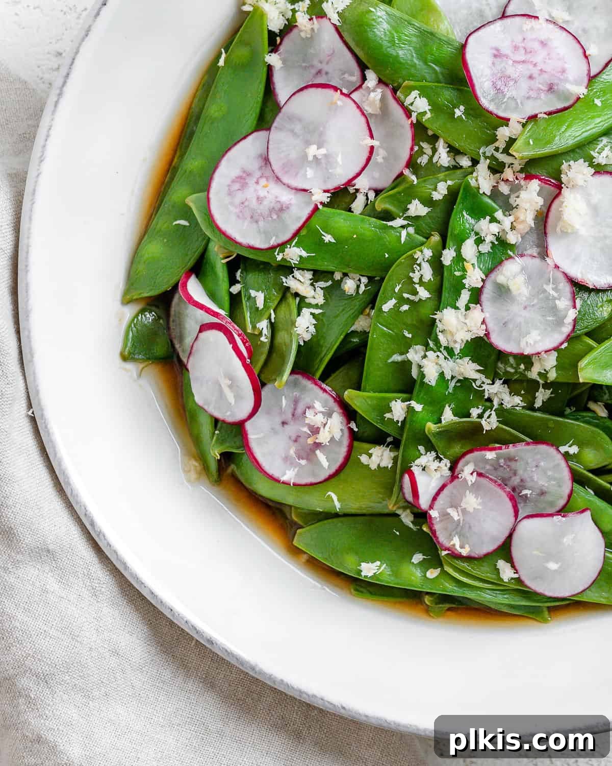 Sugar Snap Peas with Horseradish Fire 2 A bowl of vibrant green Spicy Sugar Snap Peas with Horseradish, garnished with fresh radishes, sits on a white surface, ready to be served.