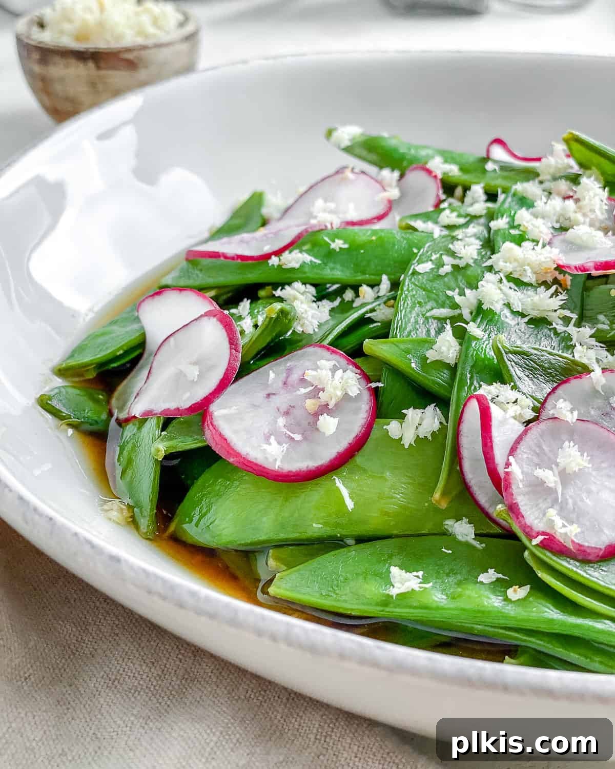 Sugar Snap Peas with Horseradish Fire 12 An appetizing close-up of Spicy Sugar Snap Peas with Horseradish in a white bowl, highlighted by natural light, showing the texture and vibrant colors of the ingredients.