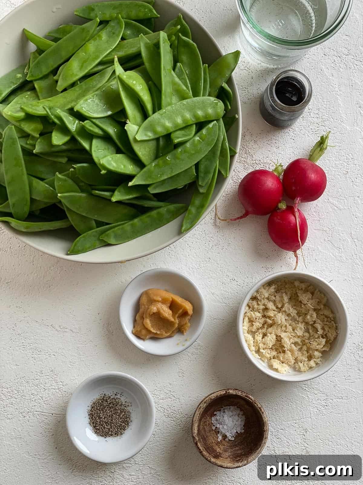 Sugar Snap Peas with Horseradish Fire 3 Measured ingredients for Spicy Sugar Snap Peas with Horseradish, including fresh peas, horseradish root, miso, and sliced radishes, laid out on a white surface.