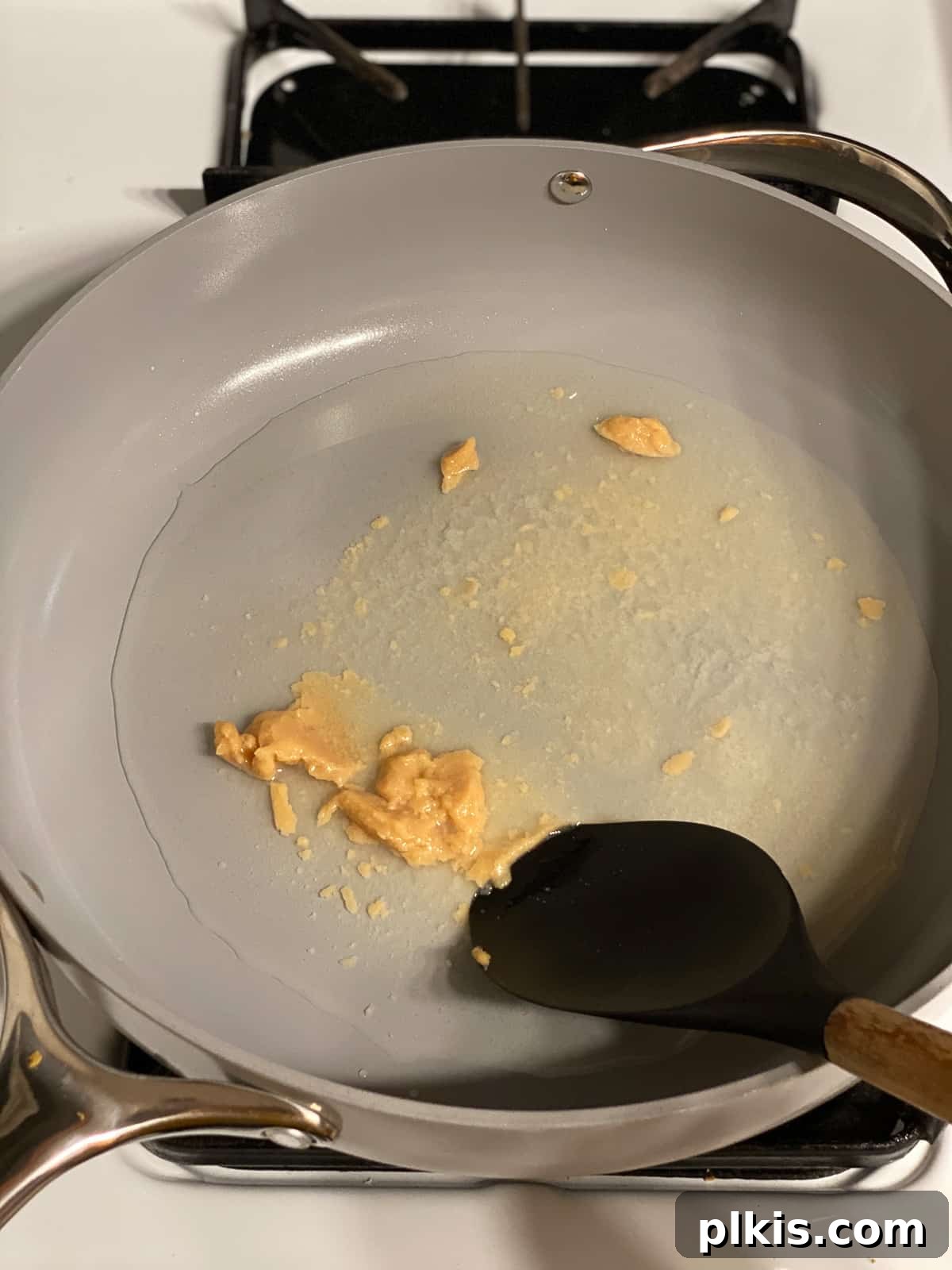 Sugar Snap Peas with Horseradish Fire 8 A hand stirring white miso paste into water in a skillet, ensuring it dissolves completely to form a smooth broth.