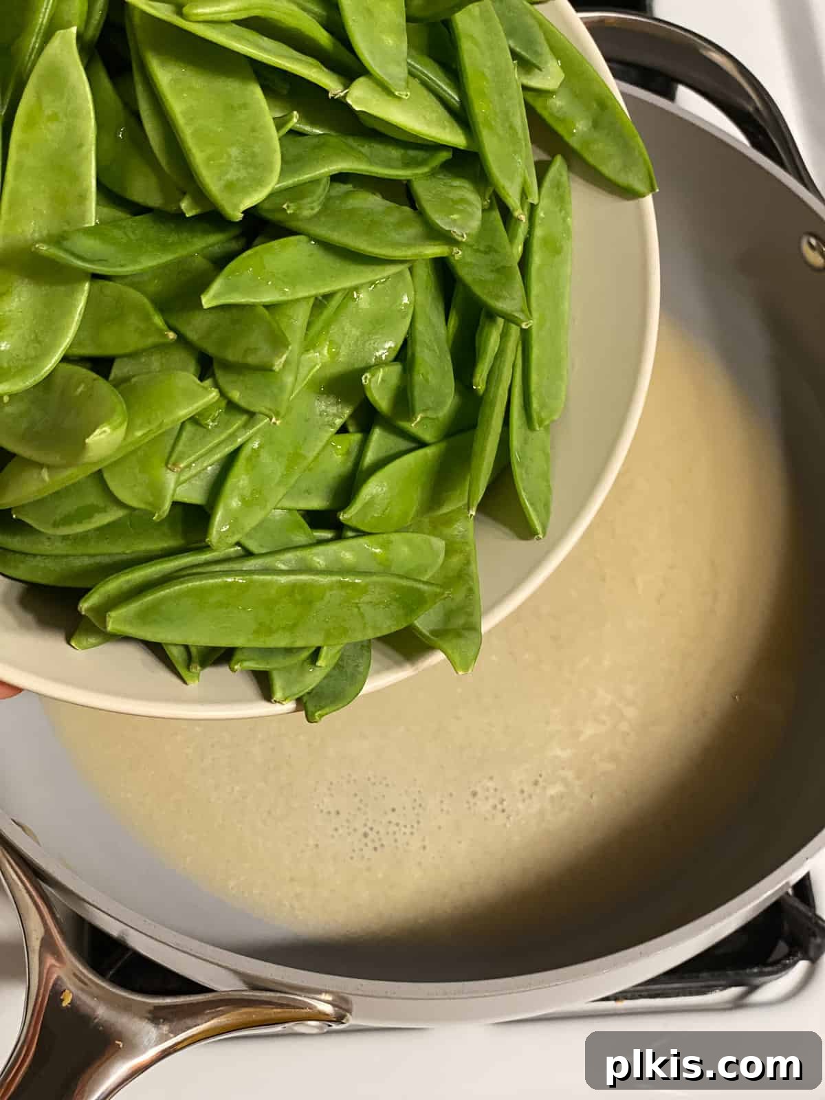Sugar Snap Peas with Horseradish Fire 9 Fresh sugar snap peas being added to the boiling miso mixture in a skillet, ready to be cooked.