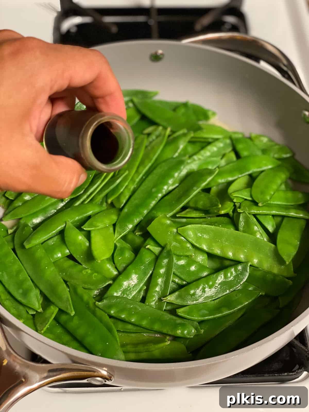 Sugar Snap Peas with Horseradish Fire 10 Soy sauce being poured into the skillet with the cooked sugar snap peas and miso mixture, ready for final stirring.