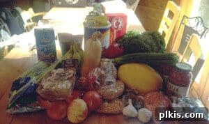 Budget Plant-Based Challenge for Two Week 2 2 Fresh weekly groceries, including vegetables, fruits, and pantry staples, neatly arranged on a kitchen table for a plant-based budget meal plan.
