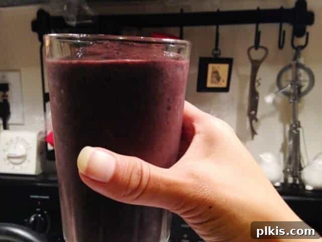 Frugal Vegan Feasts for One: Week 2 Progress 12 A hand holding a glass filled with blueberry kale smoothie.