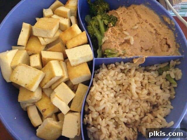 Solo Budget Plant Based Challenge Week 3 16 A divided dish containing cubed tofu, peanut sauce, and brown rice.
