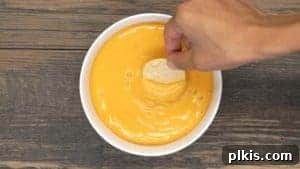 Nutritional Yeast: The Flavor-Boosting, Health-Hacking Kitchen Staple 2 A chip being dipped into a bowl of vegan nacho cheese.