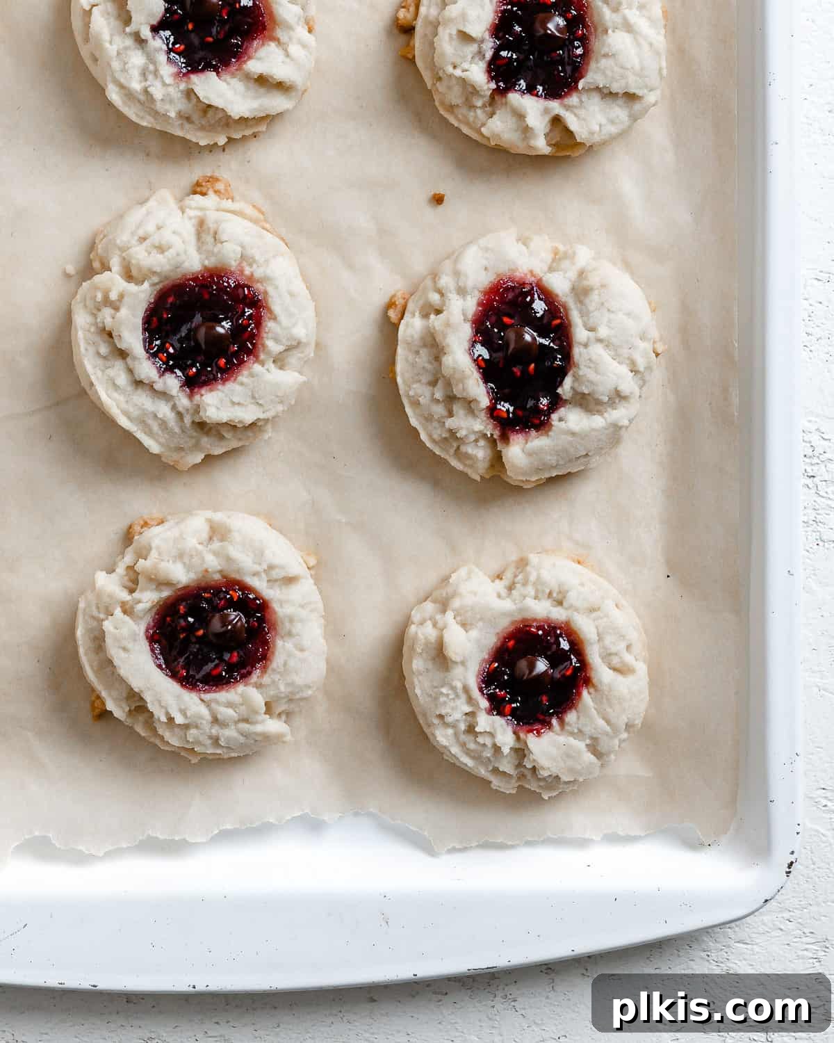 24 Festive Vegan Christmas Cookie Delights 6 Completed Raspberry Jam Thumbprint Cookies scattered on a baking sheet.