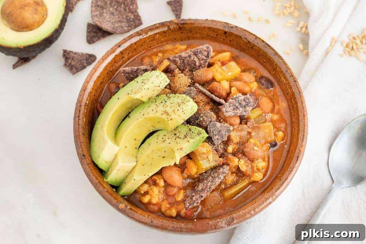 23 Soul-Soothing Vegan Soup Recipes 18 Stoneware bowl of bean and barley soup topped with crushed corn chips and sliced avocado.