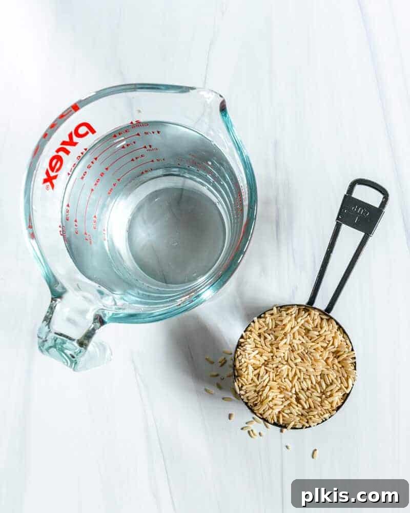 Guide to Cooking Brown Rice Liquid Measuring Cup with Water and a Cup Measurement With UnCooked Brown Rice On a Marble White Surface