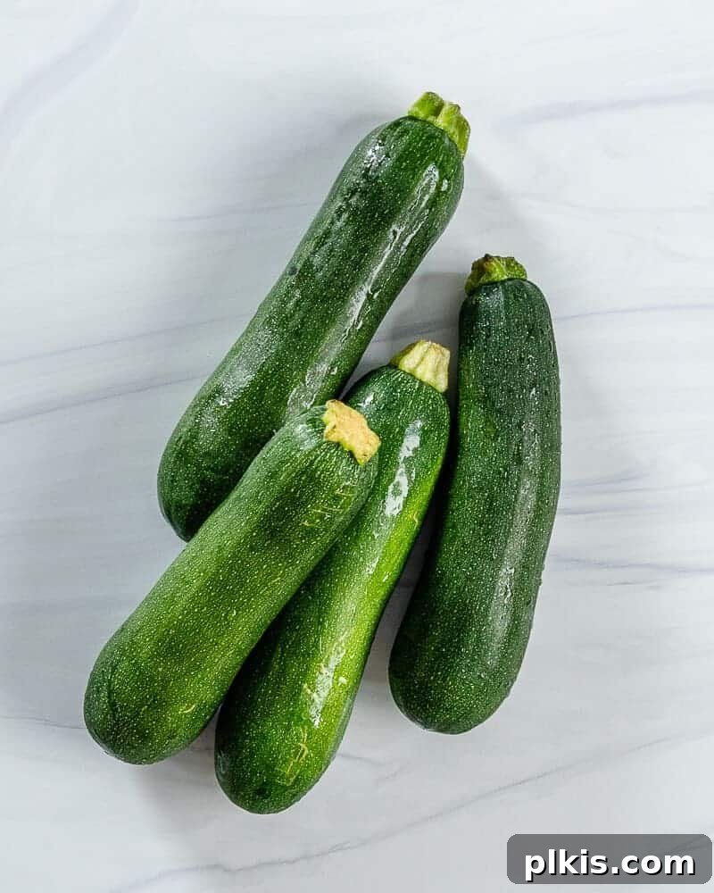 14 Zucchini Recipes You'll Crave 2 Four raw, green zucchinis arranged on a clean white background, highlighting their freshness and readiness for cooking.