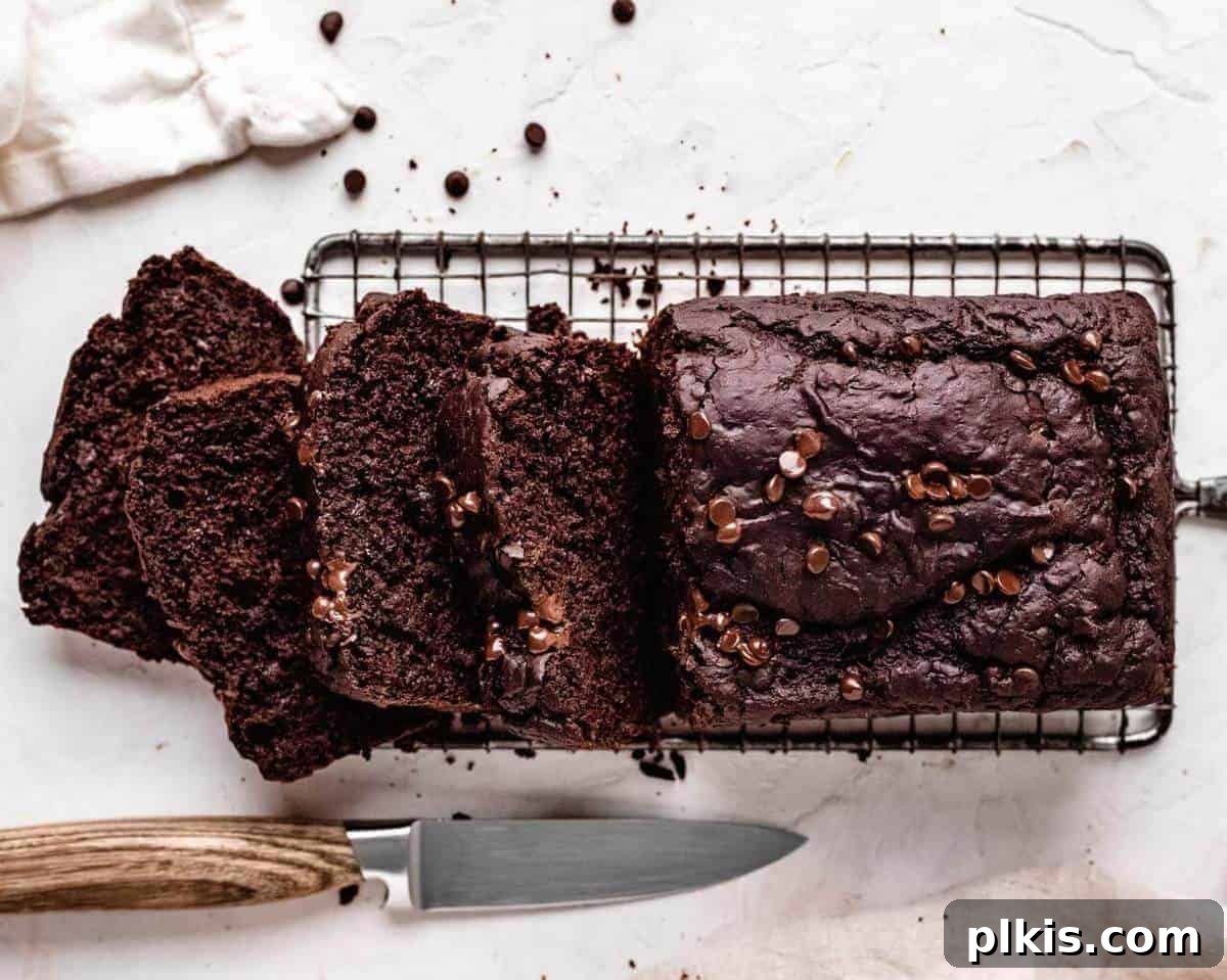 Vegan Chocolate Zucchini Bread Slices of rich vegan chocolate zucchini bread cooling on a wire rack, with a knife and white background.