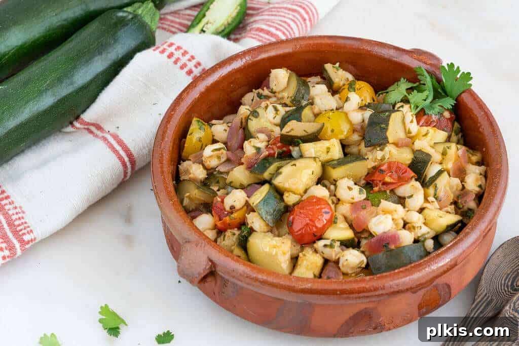 Zucchini and Hominy A rustic brown bowl filled with a savory blend of zucchini and hominy, set against a red and white cloth on a pristine white background.