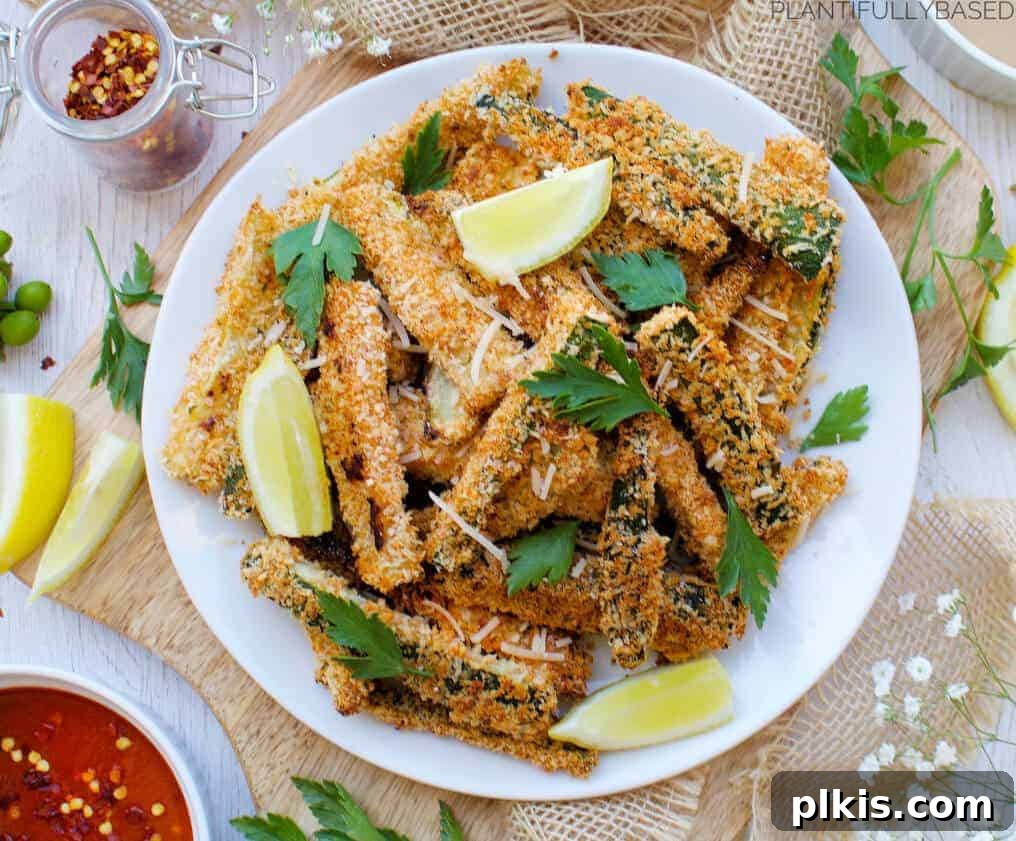 Baked Zucchini Fries A clean white plate showcasing baked zucchini fries, with various ingredients scattered in the background, suggesting a fresh and healthy preparation.