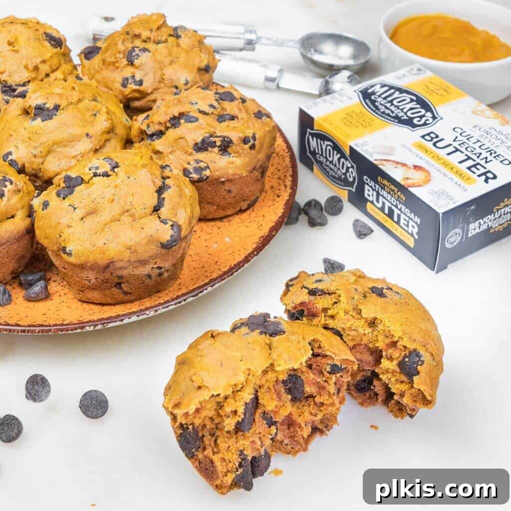 24 Effortless Plant-Based Pumpkin Creations from a Can 12 Several golden pumpkin muffins arranged on an orange plate, with one split in the foreground to show its fluffy interior, against a white background.