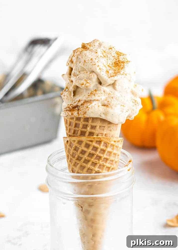 24 Effortless Plant-Based Pumpkin Creations from a Can 37 A scoop of rich pumpkin ice cream served in a cone, artfully placed within a glass jar, set against a pristine white background.