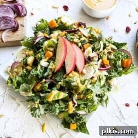 A smaller image of the finished pumpkin tahini autumn salad against a white surface, with ingredients scattered in the background.