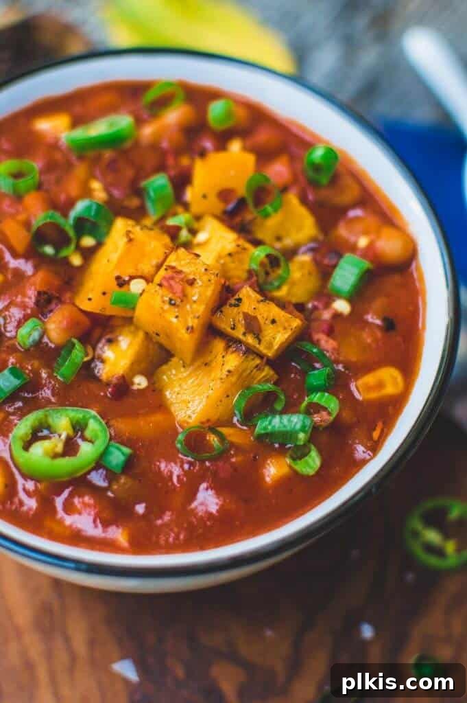 24 Effortless Plant-Based Pumpkin Creations from a Can 6 A hearty bowl of pumpkin chili, garnished and ready to be enjoyed, set against a rustic brown surface.