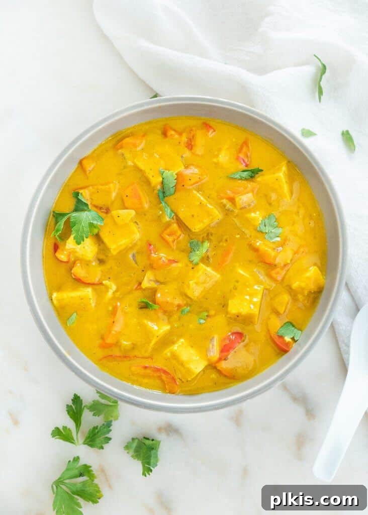 24 Effortless Plant-Based Pumpkin Creations from a Can 8 A vibrant bowl of pumpkin tofu curry, richly colored and garnished, presented against a white marble background.