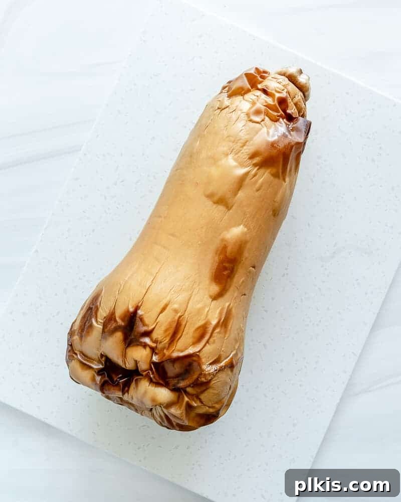 A whole roasted butternut squash, perfectly golden and tender, sitting on a baking sheet, ready to be cut and served.