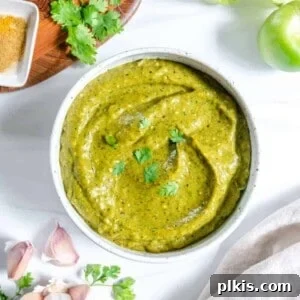 completed Creamy Tomatillo Avocado Salsa Verde in a white bowl against a white background with ingredients in the background