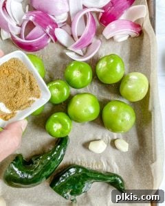 Velvety Tomatillo Avocado Verde 4 Process of adding spices to ingredients in a baking tray with parchment paper.