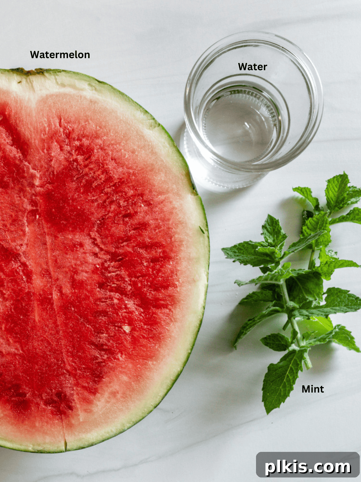 Frosty Watermelon Delight 3 Arrangement of ingredients for watermelon slushie on a white surface, including cubed watermelon, fresh mint sprigs, and a measuring spoon for water.