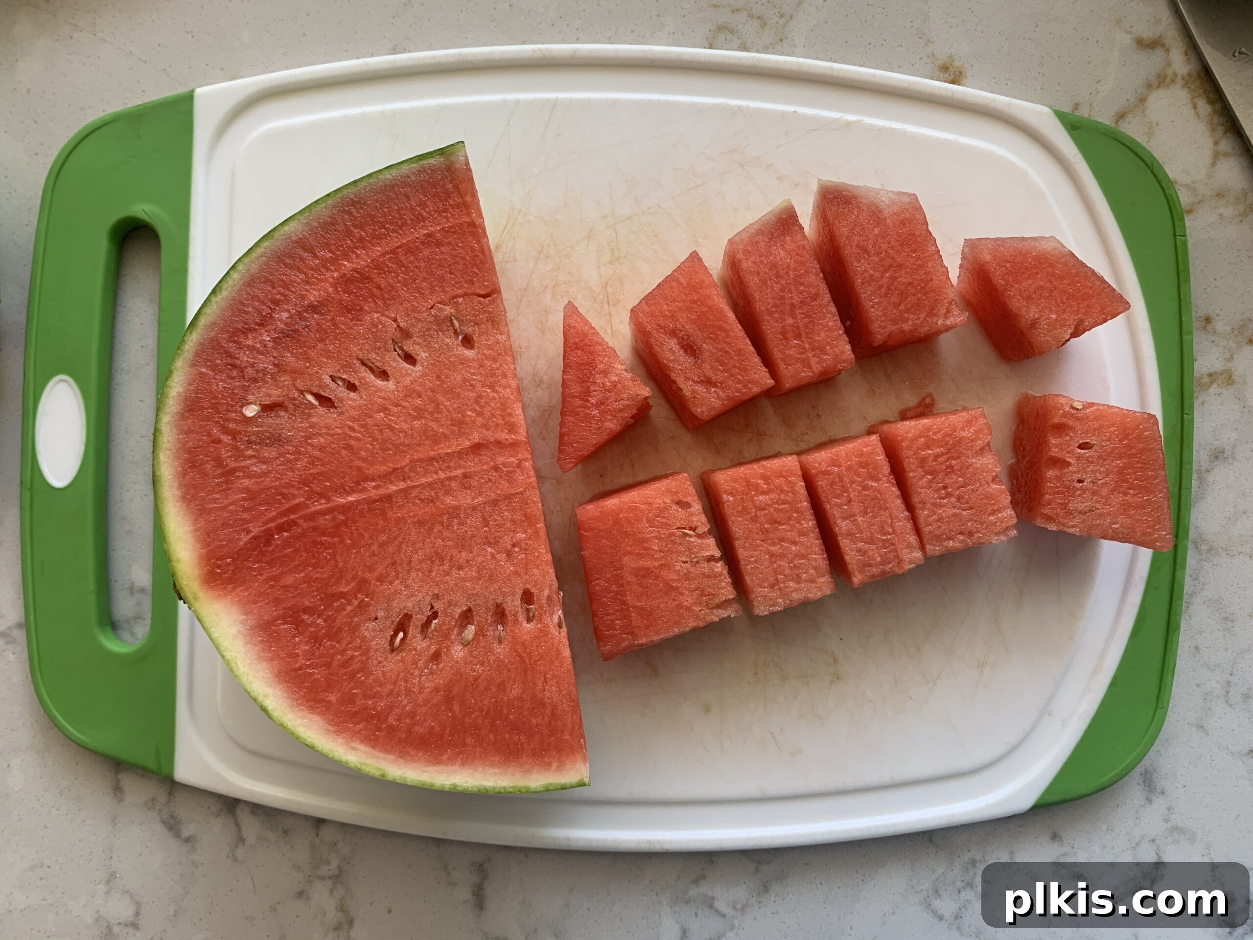 Frosty Watermelon Delight 4 Fresh watermelon being cut into cubes on a wooden cutting board, with the rind already removed.