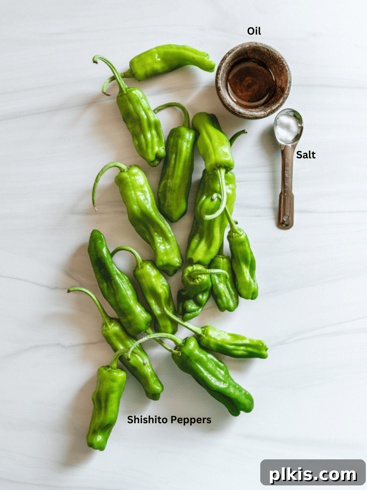 Ingredients for Blistered Shishito Peppers measured out on a white surface, including peppers, oil, and salt.