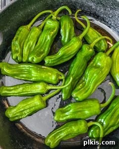 Shishito peppers being added to a hot pan with oil.