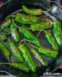 Cooked shishito peppers, visibly blistered and charred, in a pan.