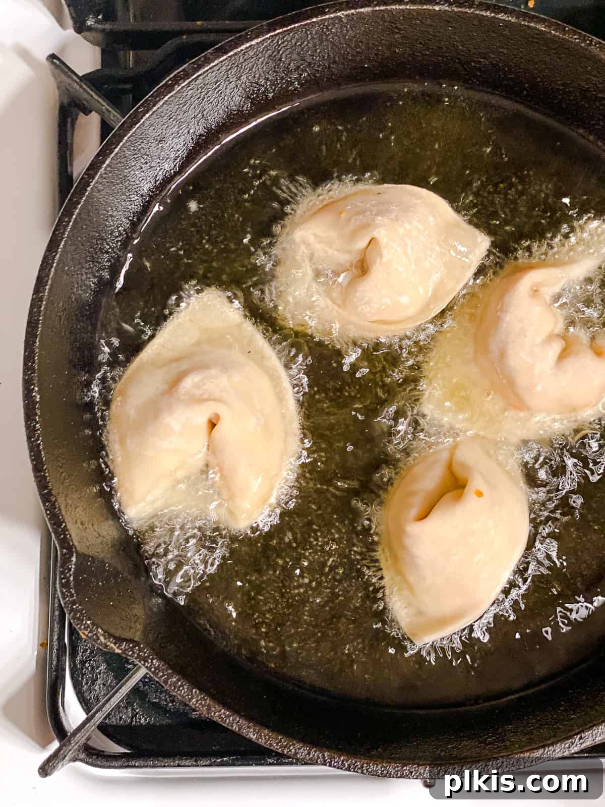 Golden Crispy Tofu Vegetable Wontons Made Two Ways 13 Process shot of several Tofu Vegetable Crispy Wontons being carefully lowered into hot oil in a deep skillet for deep-frying, showing the oil bubbling around them.