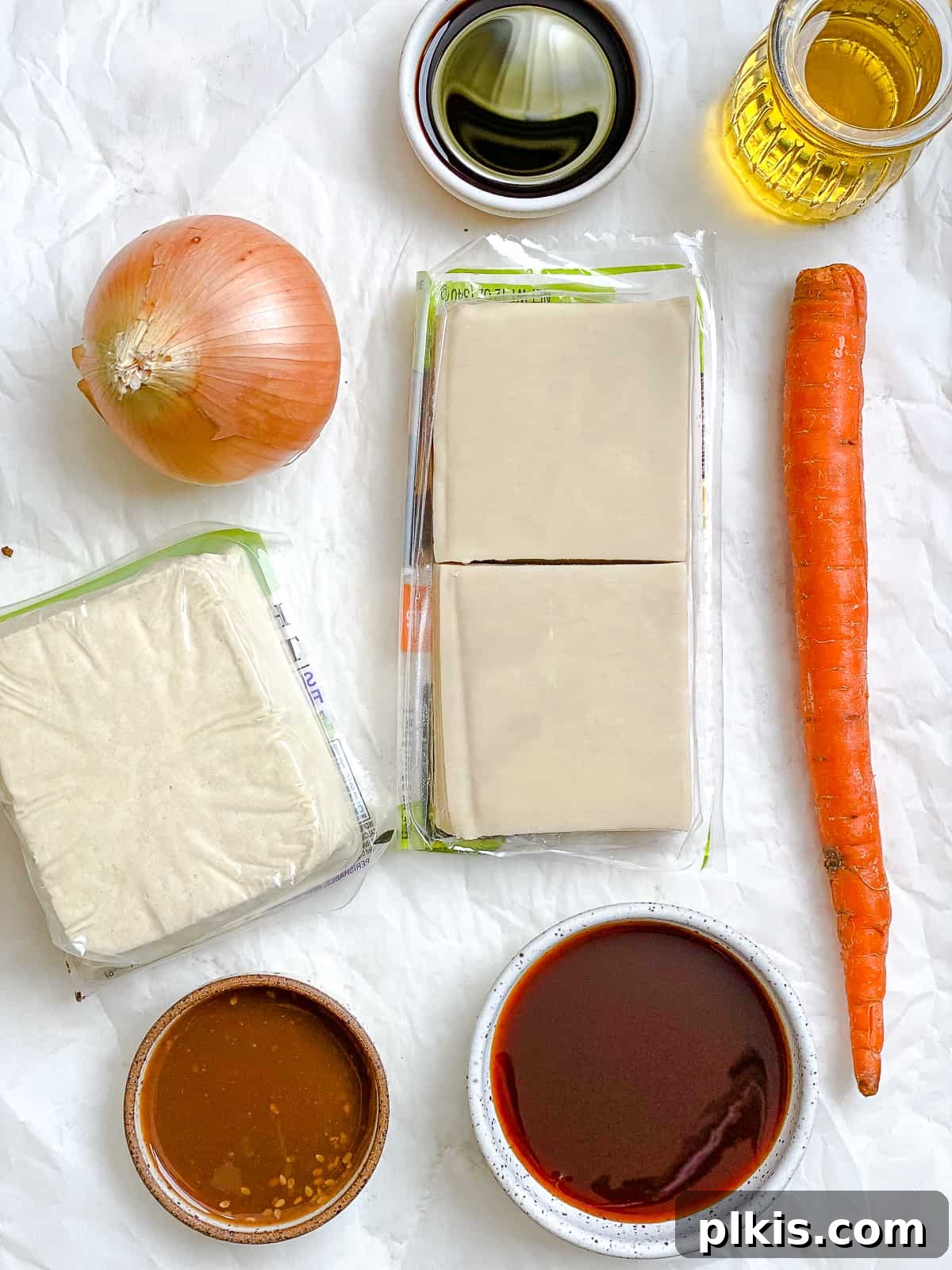 Golden Crispy Tofu Vegetable Wontons Made Two Ways 3 A curated display of fresh ingredients for Tofu Vegetable Crispy Wontons, including chopped vegetables, pressed tofu, sauces, and wonton wrappers, all neatly arranged on a white surface.