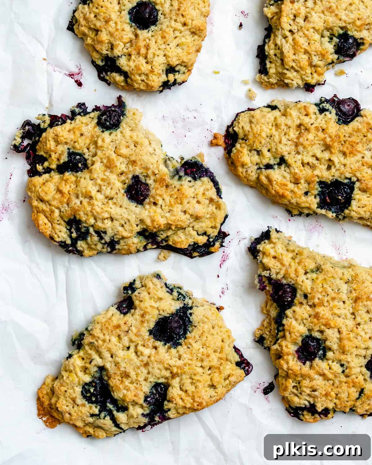 Sunshine Lemon Blueberry Plant-Based Scones 2 Completed Vegan Lemon Blueberry Scones scattered on a white surface, showcasing their golden crust and juicy berry flecks.