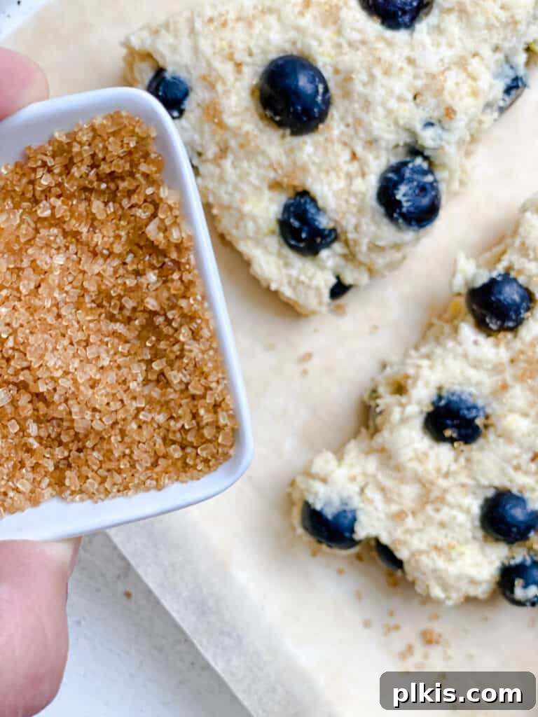 Sunshine Lemon Blueberry Plant-Based Scones 11 A process shot showing a hand brushing plant-based milk onto an unbaked scone, preparing it for a sugar sprinkle.