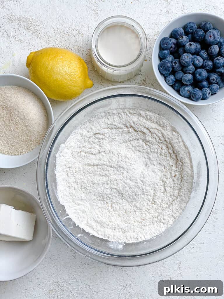 Sunshine Lemon Blueberry Plant-Based Scones 5 A close-up of ingredients for Vegan Lemon Blueberry Scones, including a pile of flour, sugar, and baking powder, laid out on a white surface.