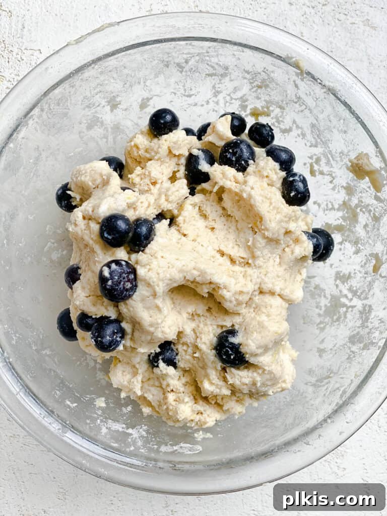 Sunshine Lemon Blueberry Plant-Based Scones 7 A process shot of mixed scone dough with visible blueberries in a clear glass bowl, illustrating the texture before shaping.
