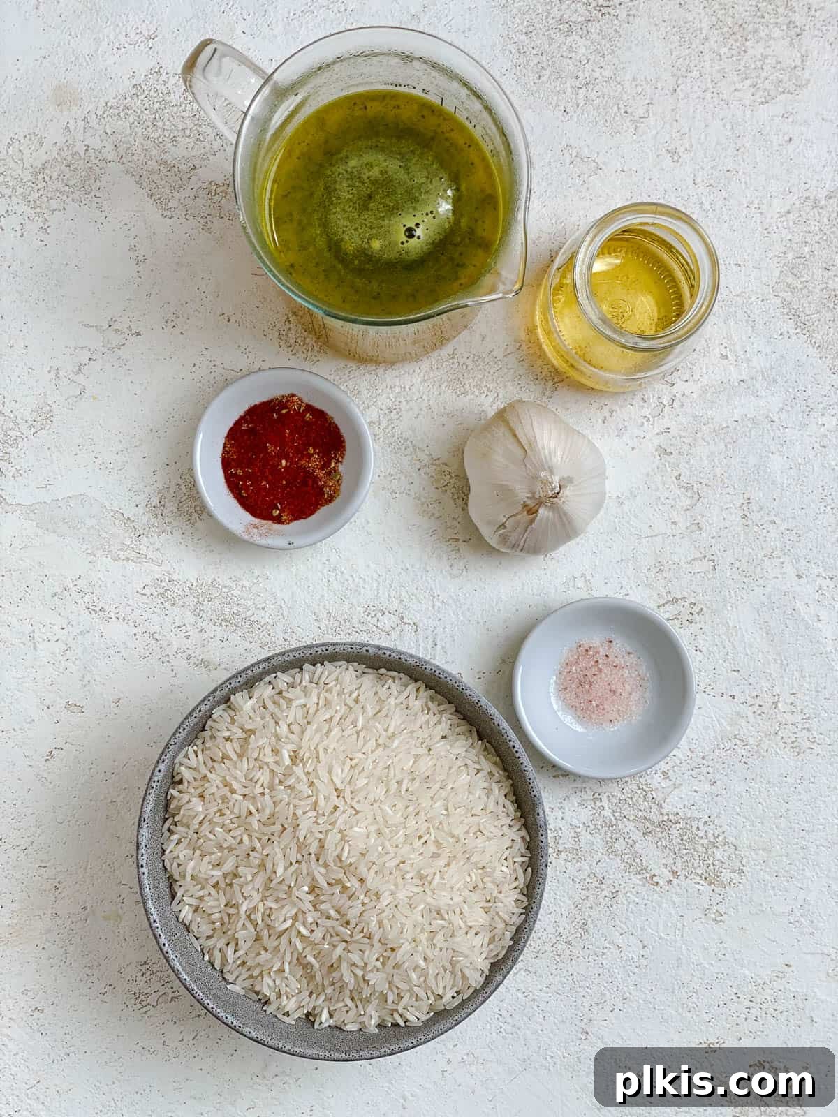 Neatly arranged ingredients for preparing Golden Garlic Rice [Spanish Yellow Rice] on a clean white surface, showcasing the fresh garlic, rice, achiote powder, and other essential components.