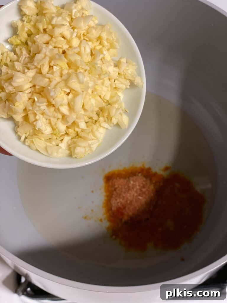 Aromatic Garlic Rice 6 Process shot demonstrating the addition of minced garlic to a pan with oil and achiote powder, releasing its aromatic fragrance.